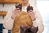 Crop unrecognizable female in apron showing baked dessert in paper liners in house kitchen