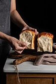 Unbekannter Erntebäcker, der geteilte Hälften von Sandwichbrot von der Grillplatte auf dem Tresen im gedämpften Licht nimmt