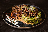 Yummy vegan dish with zucchini spaghetti and sauteed mushroom slices covered with red berries and alfalfa sprouts on dark background