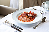 From above of assorted jamon and chorizo slices served on white plate and placed on round table with coffee cup and cutlery in elegant restaurant