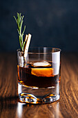 Glass of whiskey with rosemary placed on wooden table