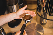 High angle of crop anonymous male barista preparing ground coffee in portafilter for making espresso in cafe