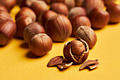 Closeup fresh hazelnut with cracked shell placed near bunch of ripe nuts on yellow background