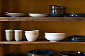Set of various dishware consisting of plates cups and bowls placed on wooden shelves