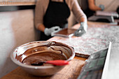 Soft focus of bowl with liquid chocolate and spoon placed on table near digital scale and confectioner