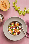 From above exotic melon, mozzarella and prosciutto salad on pink colorful background