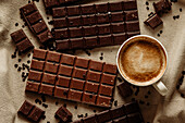 From above cup of hot aromatic coffee placed on wooden table near set of chocolate bars with