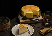 From above plates with tasty cotton cheesecake placed near glass of beverage on wooden table in dark room