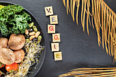 Draufsicht auf dekorativen Titel neben Teller mit gekochten Kartoffeln und Grünkohlblättern auf Nüssen und Sprossen auf grauem Hintergrund