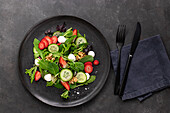 Teller mit einem Sommersalat aus Erdbeeren und Gurken auf einem dunklen Tisch