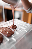 Cropped unrecognizable person in apron and gloves filling plastic mold with liquid chocolate during work in confectionery in daytime