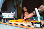 Anonyme Frau schneidet frischen, reifen Kürbis auf einem hölzernen Schneidebrett, während sie das Mittagessen in einem Wohnwagen während einer Reise in Kantabrien vorbereitet