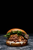Appetitlicher Burger mit frischem Salat, Käse, Mayonnaise und Schweinefleisch auf einem Tisch in einem dunklen Raum