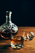Glas kalter Whiskey mit Eis auf Holztisch neben Karaffe auf schwarzem Hintergrund