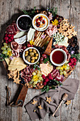 Top view of prosciutto with assorted cheese on platter with berries and cookies served on wooden table in kitchen