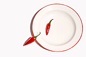 Top view composition of bowl with hot peppers with green stem placed on white background