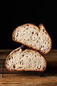Halves of tasty sourdough bread with brown crust placed on grill tray on wooden table against black backdrop