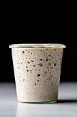 Glass white cup with sourdough starter covered with glass transparent lit placed on surface against black background