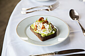 From above of healthy avocado toast with ricotta and walnuts placed on white plate and served on table in cafe during breakfast
