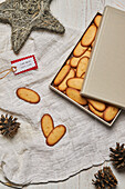 High angle of gift tag and cones placed on table with box full of homemade sweet Christmas biscuits