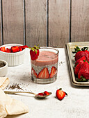 Tasty pudding with chia seeds and slices of fresh strawberries placed on table near ingredients for healthy breakfast