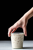 Hand of crop anonymous person demonstrating white round glass cup with sourdough starter and covered with glass lid placed on table against black background