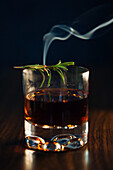 Glass of whiskey with rosemary placed on wooden table against blue background