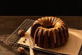 From above coffee walnut bundt cake placed on baking net on dark rustic wooden table in kitchen
