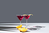 Composition of glass filled with red fruit cocktail near orange slides and zest placed on concrete table against grey background