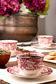 Dekorative Keramiktassen mit Kaffee, serviert auf einem Tisch mit Blumen für die Teestunde in einem gemütlichen Zimmer zu Hause