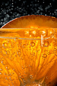 Nahaufnahme eines Gin-Tonic-Cocktails mit einer frischen Orangenscheibe, die im Glas blubbert