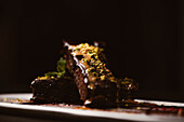 Leckere Brownies mit Erdnussbutter und knusprigen, zerstoßenen Pistazien neben einer Kugel Gelato auf einem Teller mit Schokoladensauce
