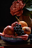 Fresh apples and peach with grapes and granadilla in bowl placed on table near red peony