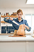 Young female with sharp knife cutting raw squash on chopping board while cooking in kitchen at home