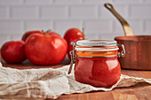 Glass jar with fresh tomato sauce placed on woven mat in kitchen at home