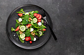 Dish with a summer salad of strawberries and cucumber on a dark table