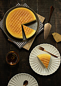 From above plates with tasty cotton cheesecake placed near glass of beverage on wooden table in dark room