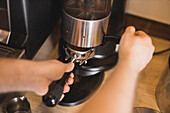 High angle of crop anonymous barista preparing fresh ground coffee in portafilter of professional grinder in cafe