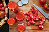 Top view of ripe red tomatoes and jars of sauce placed on table in kitchen