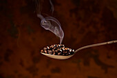Von oben Nahaufnahme eines Löffels voll mit einem Haufen gerösteter Kaffeebohnen auf braunem Hintergrund