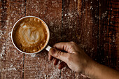 Top view of crop anonymous person with cup of aromatic coffee with foam on wooden table