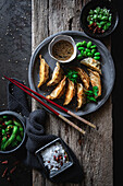 Gyozas with green beans and soy sauce with sesame seeds placed with chopsticks near bowls with spices and pea pods
