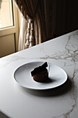 High angle of yummy chocolate glazed cake decorated with edible decoration served on white plate and placed on marble table