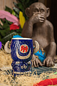 Bull shaped tiki mug of alcohol drink with froth placed against dry grass and feathers on blurred background