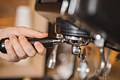 Crop anonymous male barista attaching portafilter with ground espresso coffee on coffee machine in kitchen