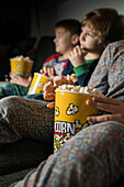 Cropped young amazed siblings kids sitting comfortable on sofa with popcorn bucket while eating and watching TV