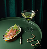 From above of appetizing smoked salmon slices served on plate with lime and onion and placed on round table with glass of vermouth with olive near elegant pearl necklace