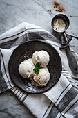 Top view of tasty gelato with fresh mint leaves and cinnamon powder on top near scooper on towel