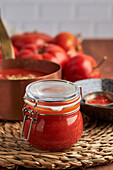 Glass jar with fresh tomato sauce placed on woven mat in kitchen at home