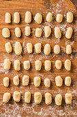 Blick von oben auf ungekochte Gnocchi, die während der Zubereitung des Mittagessens zu Hause in geordneten Reihen auf einem Holztisch liegen